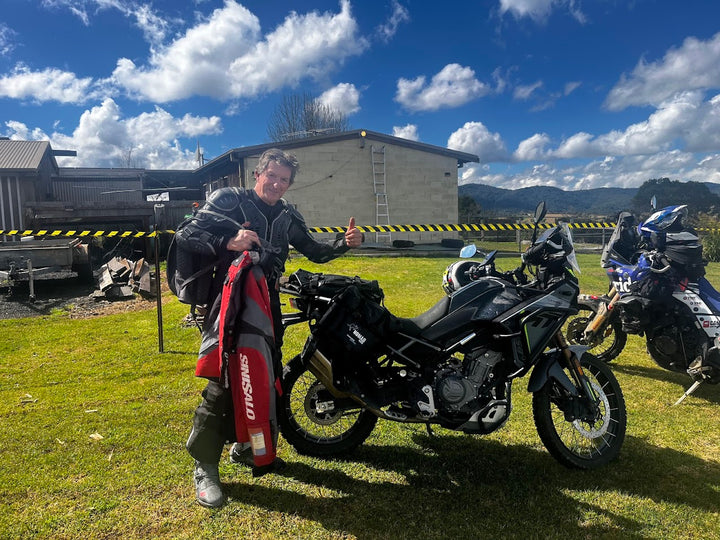 Adventure rider holding jacket beside bike