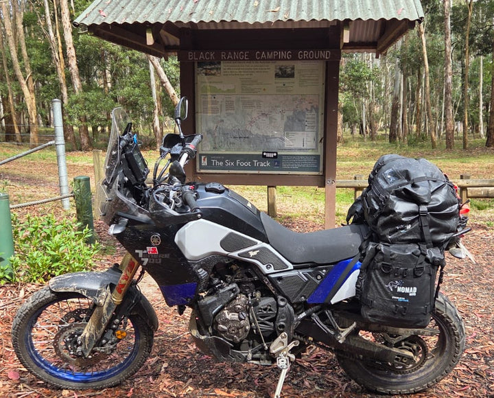 Nomad Moto Motorcycle with luggage at a camping area in a forest